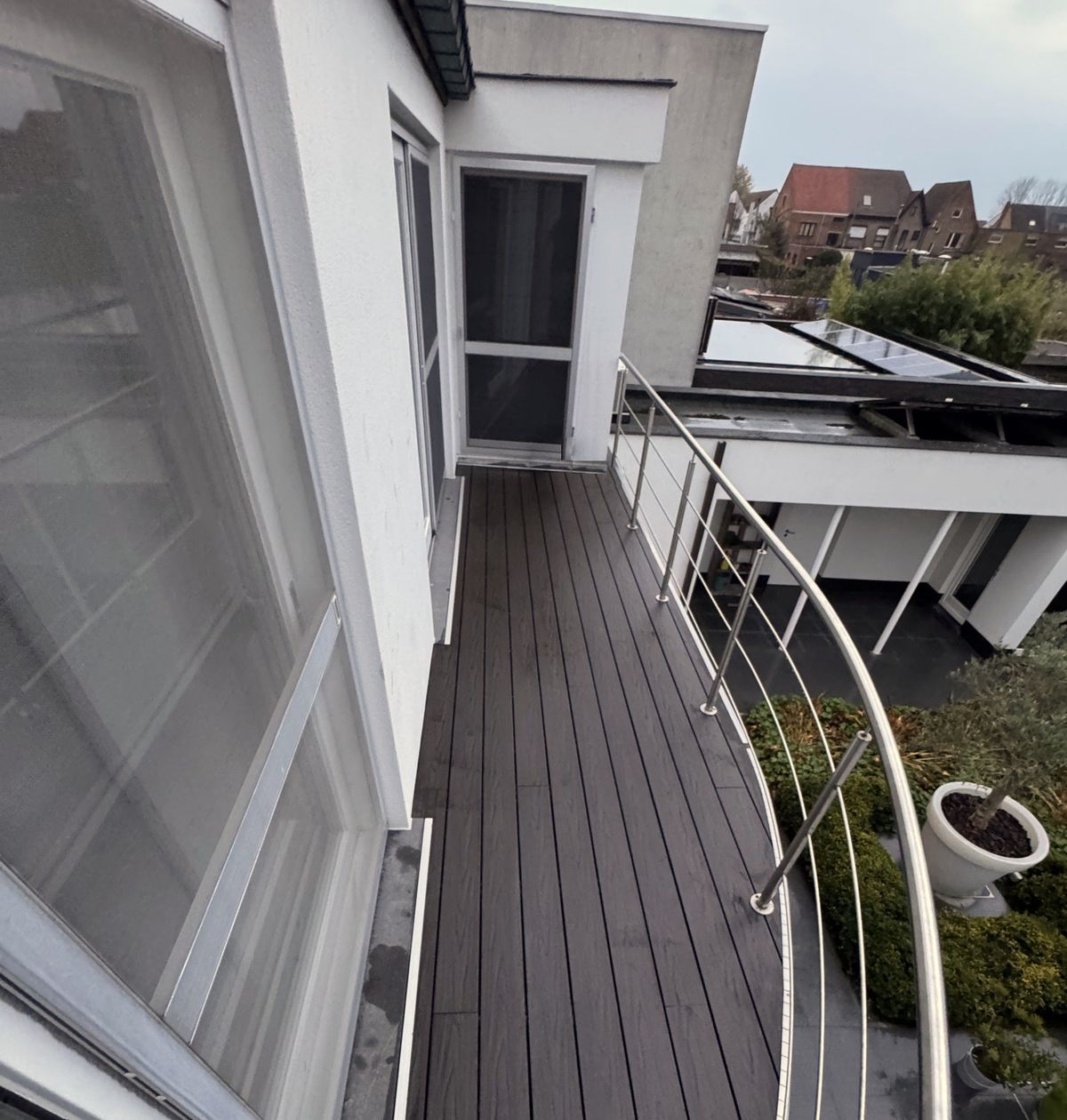Het nieuwe terras in donkere planken in de lengte gelegd, met een gebogen inox reling