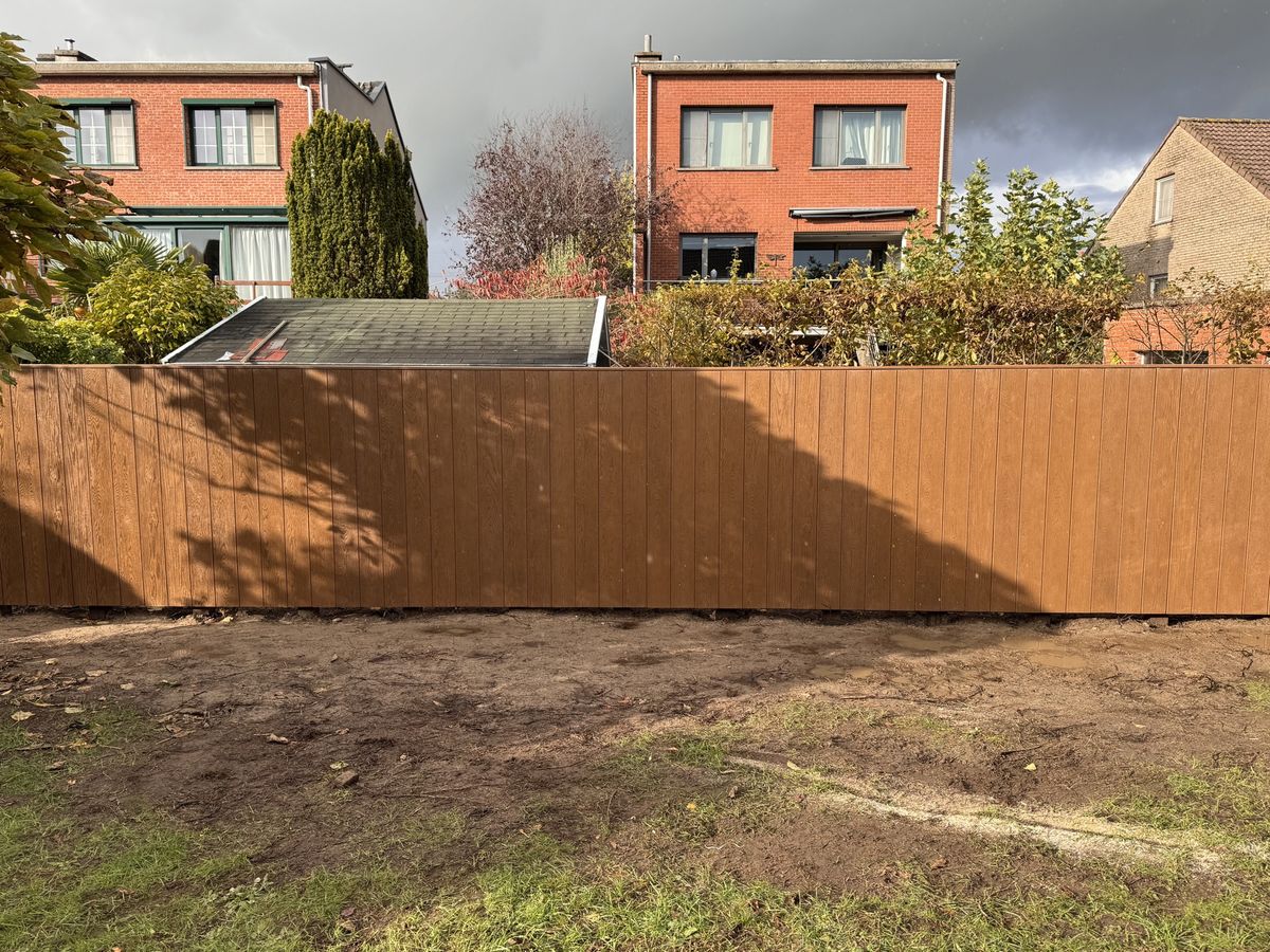 Afgewerkte tuinwand van verticale bruine planken langs de perceelgrens van een tuin