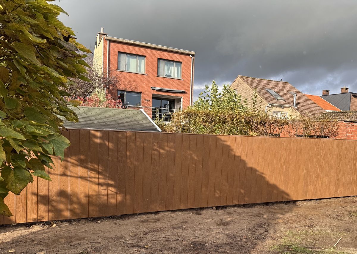 De afgewerkte tuinwand in de tuin, met een boom en woningen op de achtergrond